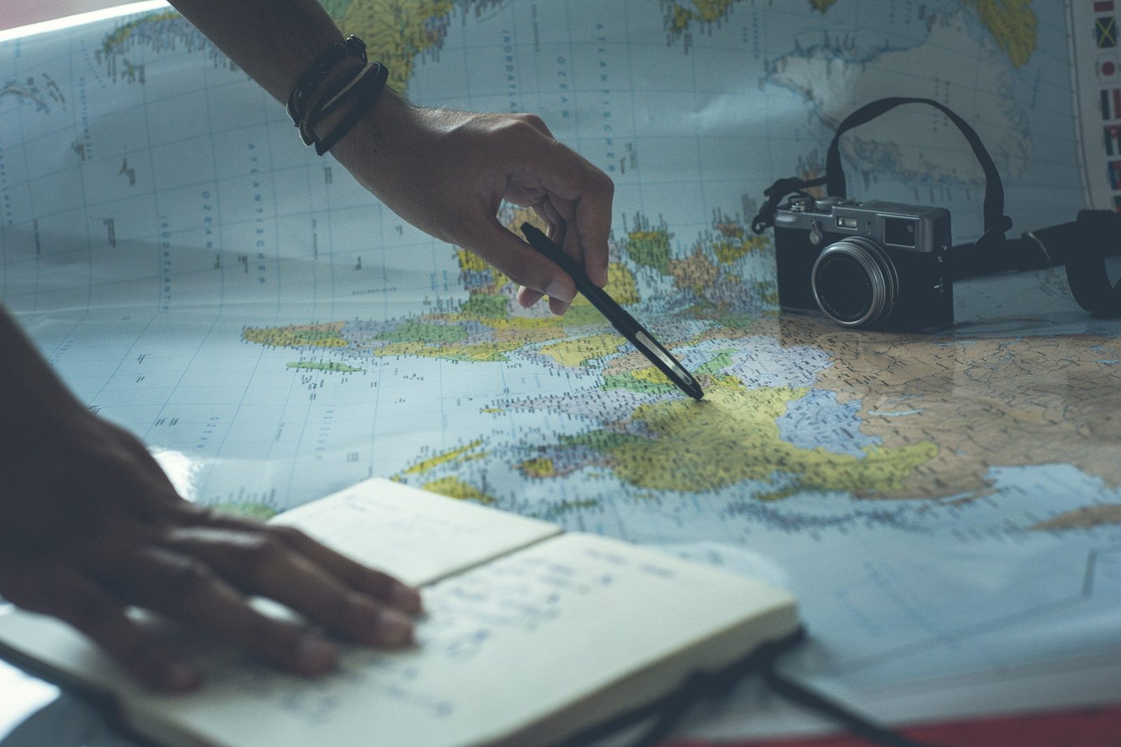 A consultant tracing a route across a map with a pen beside an open notebook