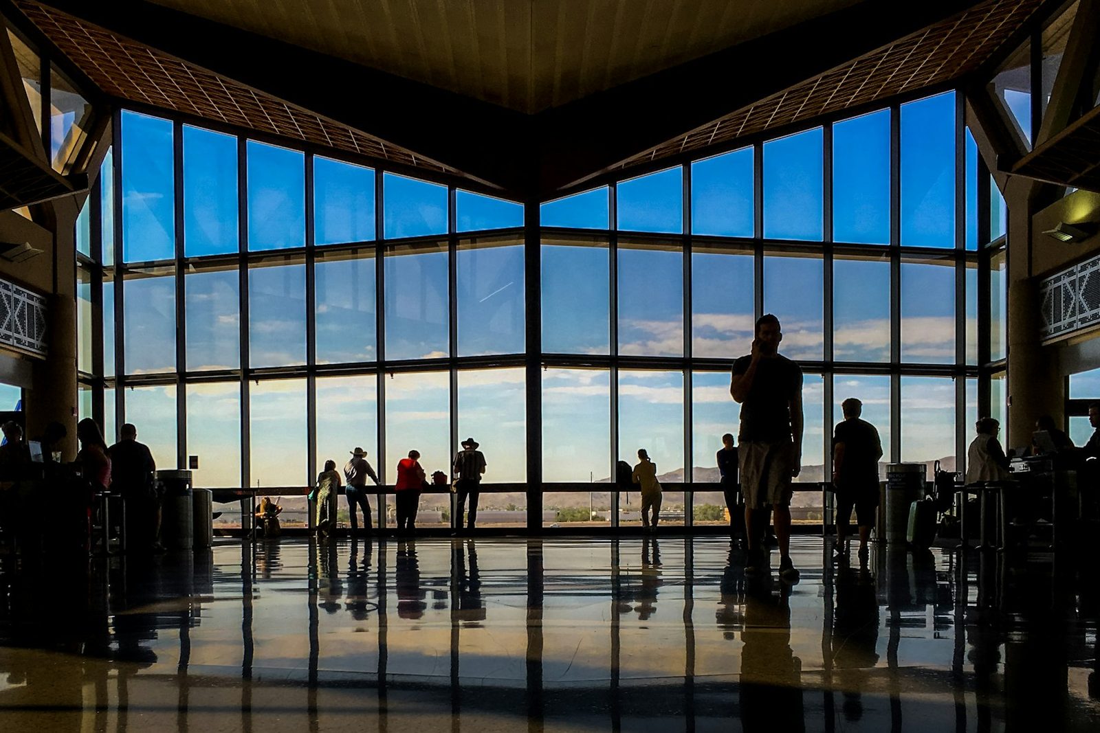 Travellers silhouetted against the tall windows of an airport departure hall