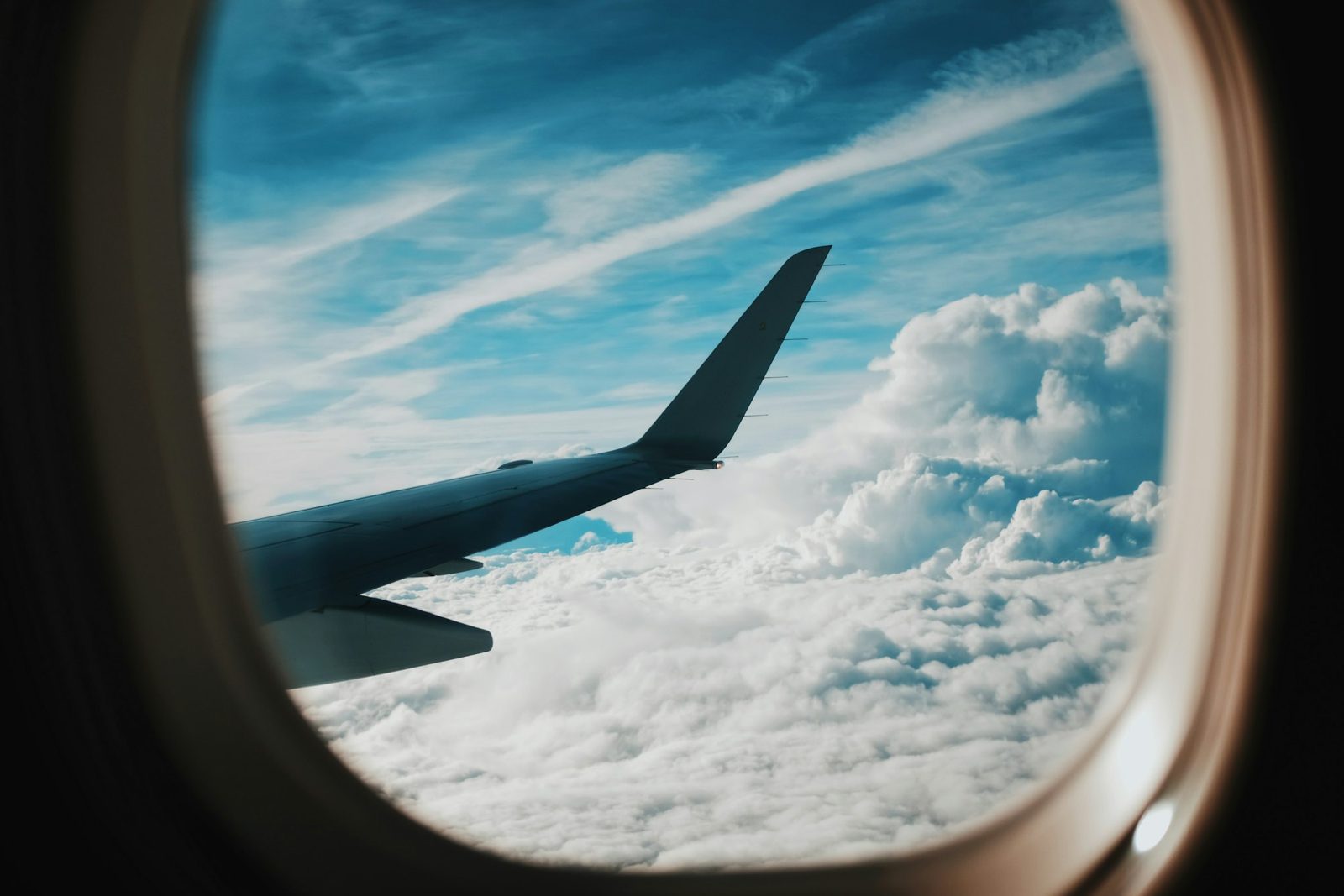 An aircraft wing above the clouds, seen through a cabin window