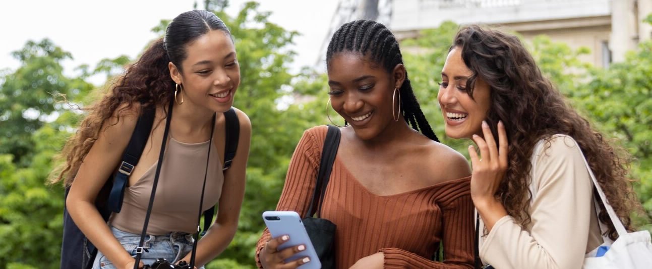 Three friends abroad laughing together over a phone
