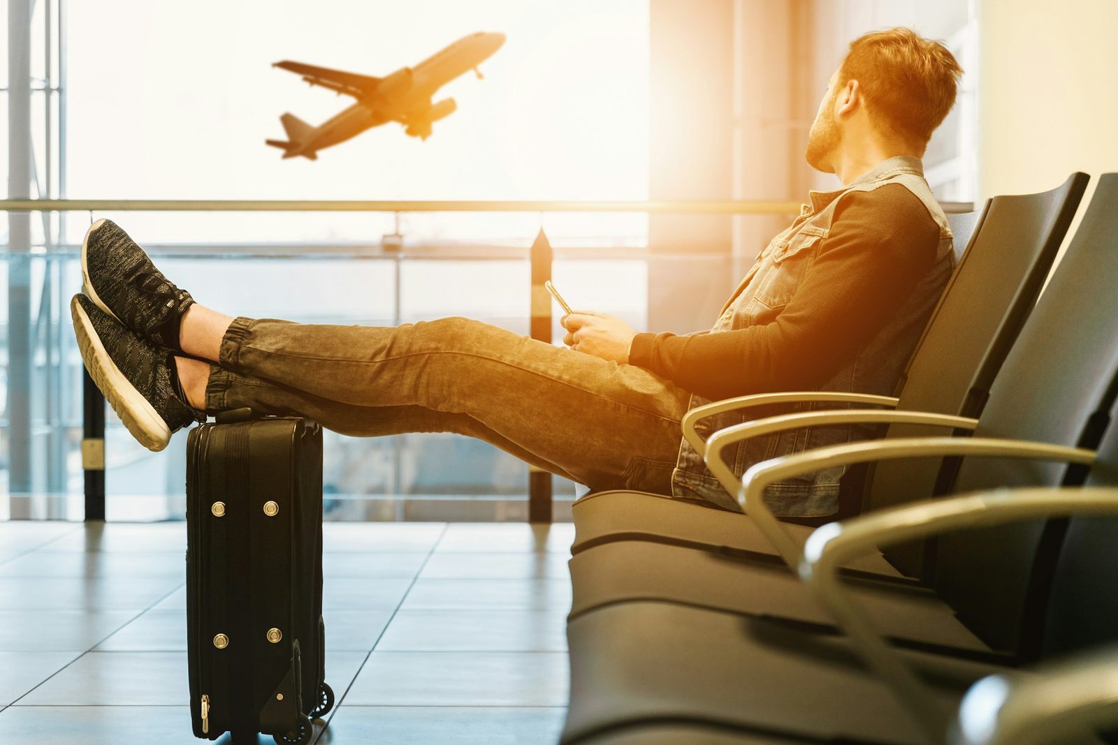 A traveller resting in an airport lounge with his feet on his suitcase as a plane takes off