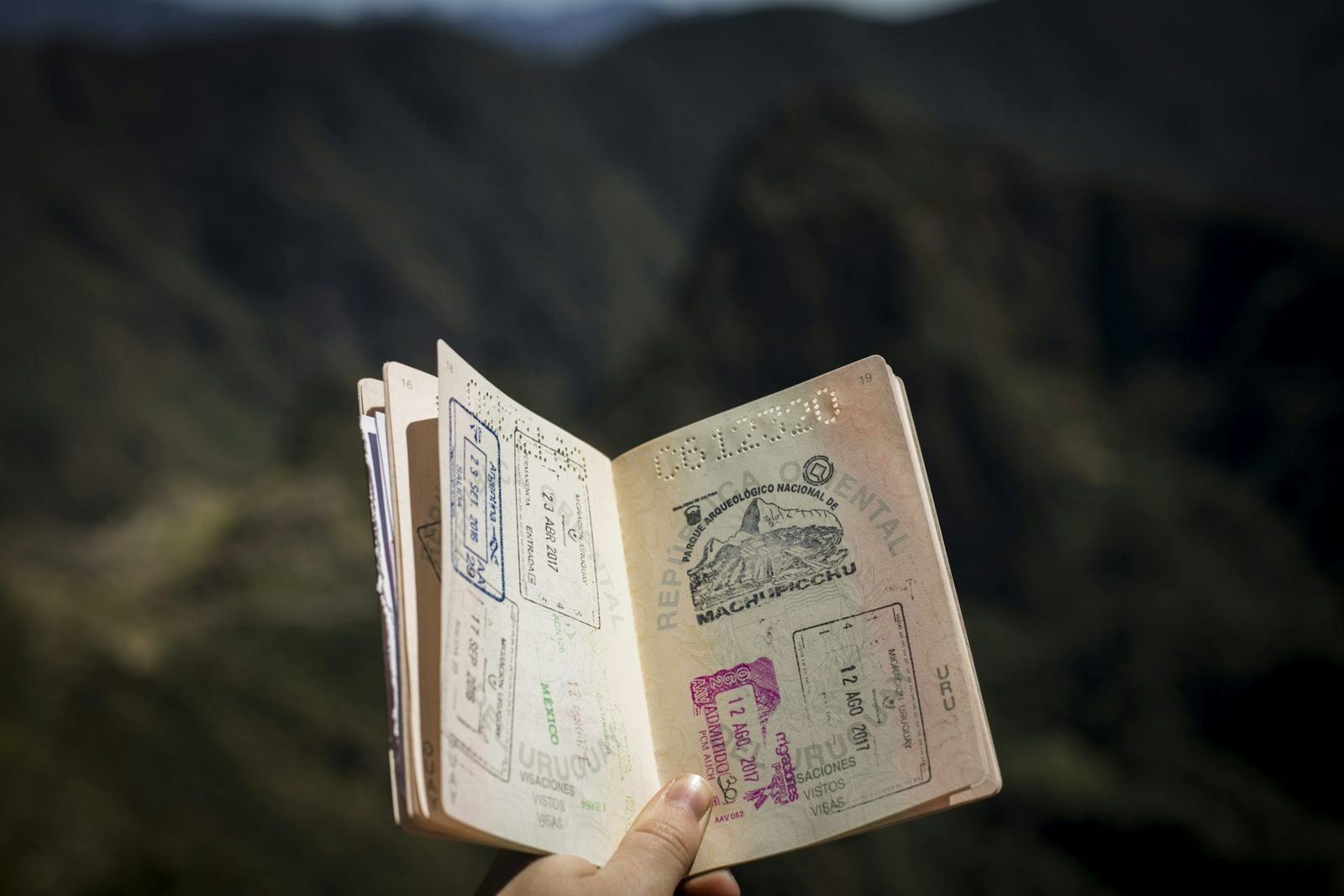 A hand holding up a well-used passport open at its stamped visa pages
